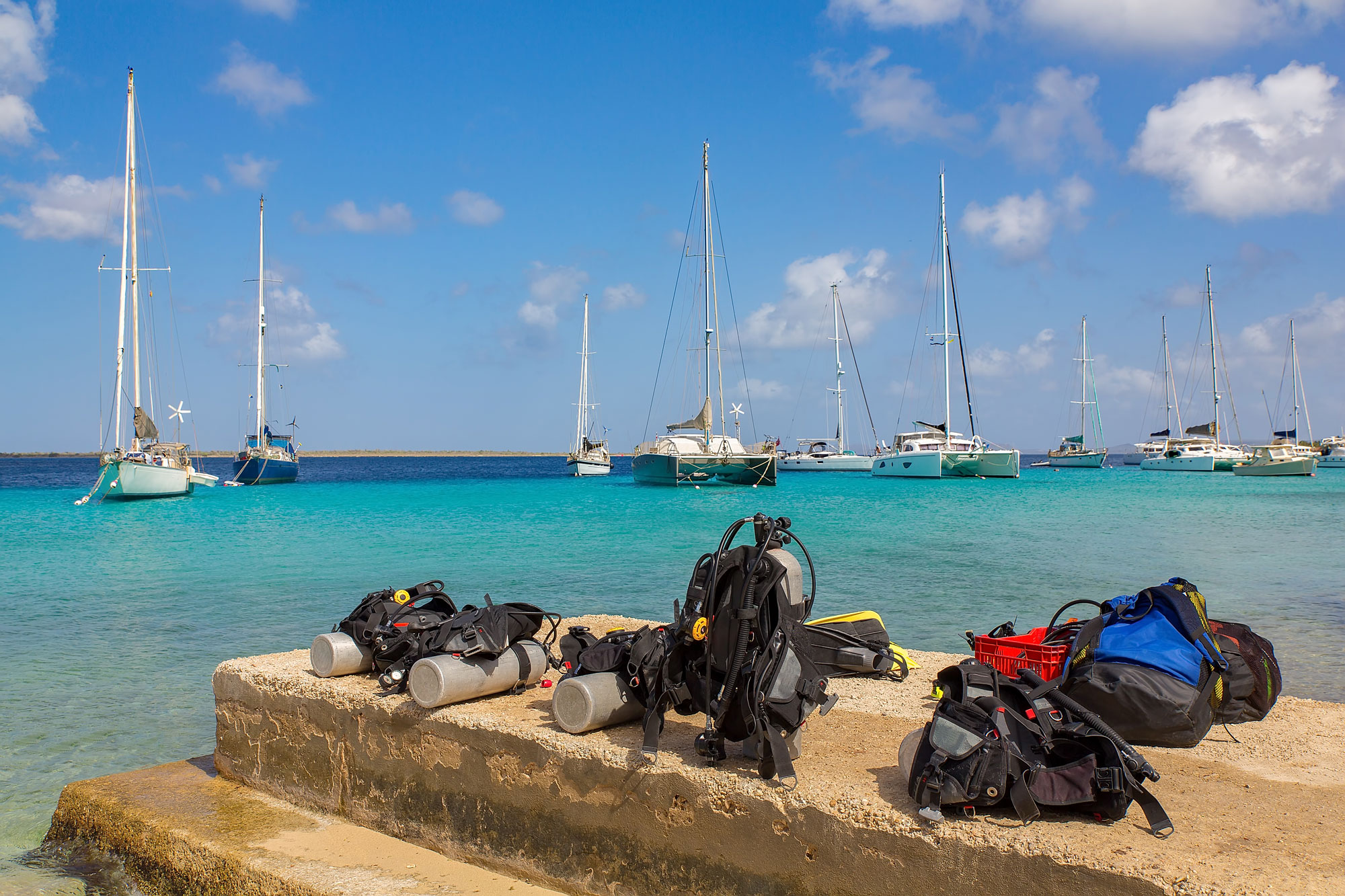 Scuba tanks on a pier with sailboats in the water in the background.