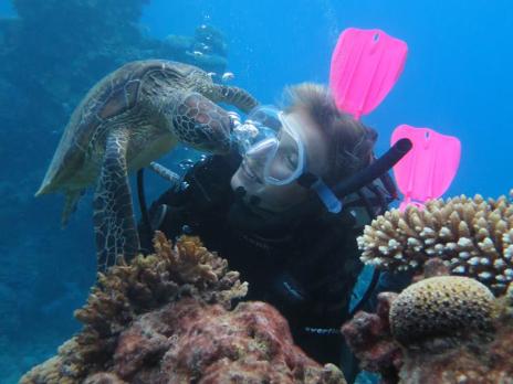 PADI AmbassaDiver Katt Andryskova taking a photo in her scuba gear with a sea turtle underwater.