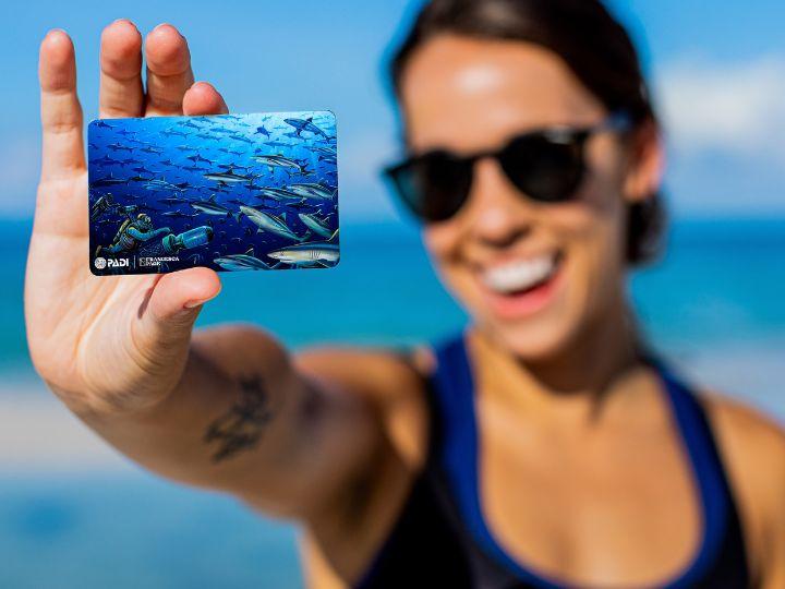woman holding a PADI certification card featuring shark illustrations