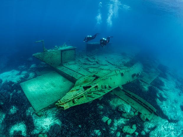 A shipwreck resting underwater as divers approach.