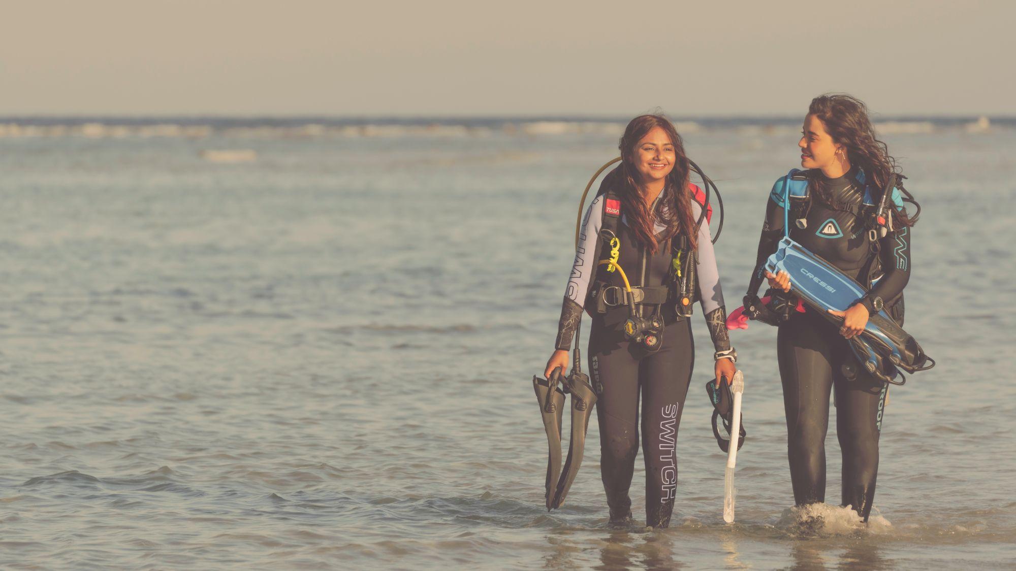 Two people walking on beach carrying scuba gear.