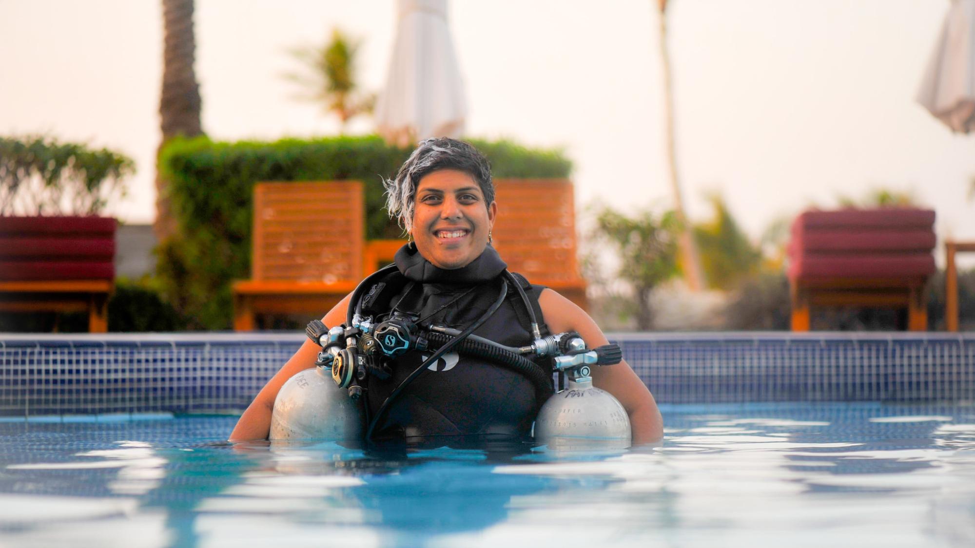 PADI AmbassaDiver Sara Gojer smiling while in her scuba diving gear above water.